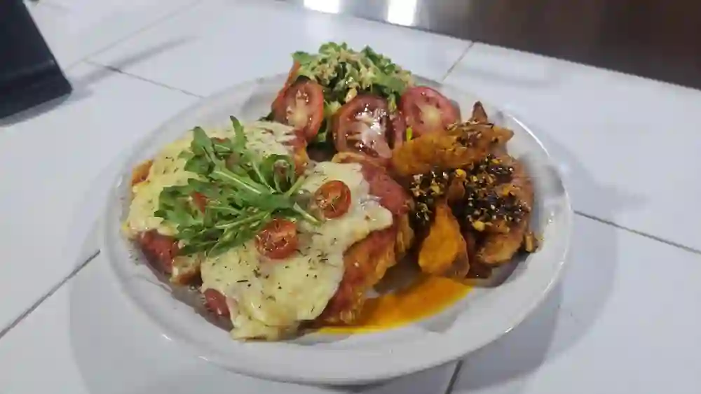 Milanesa a la parmesana con jitomate, arúgula y gajos de papa