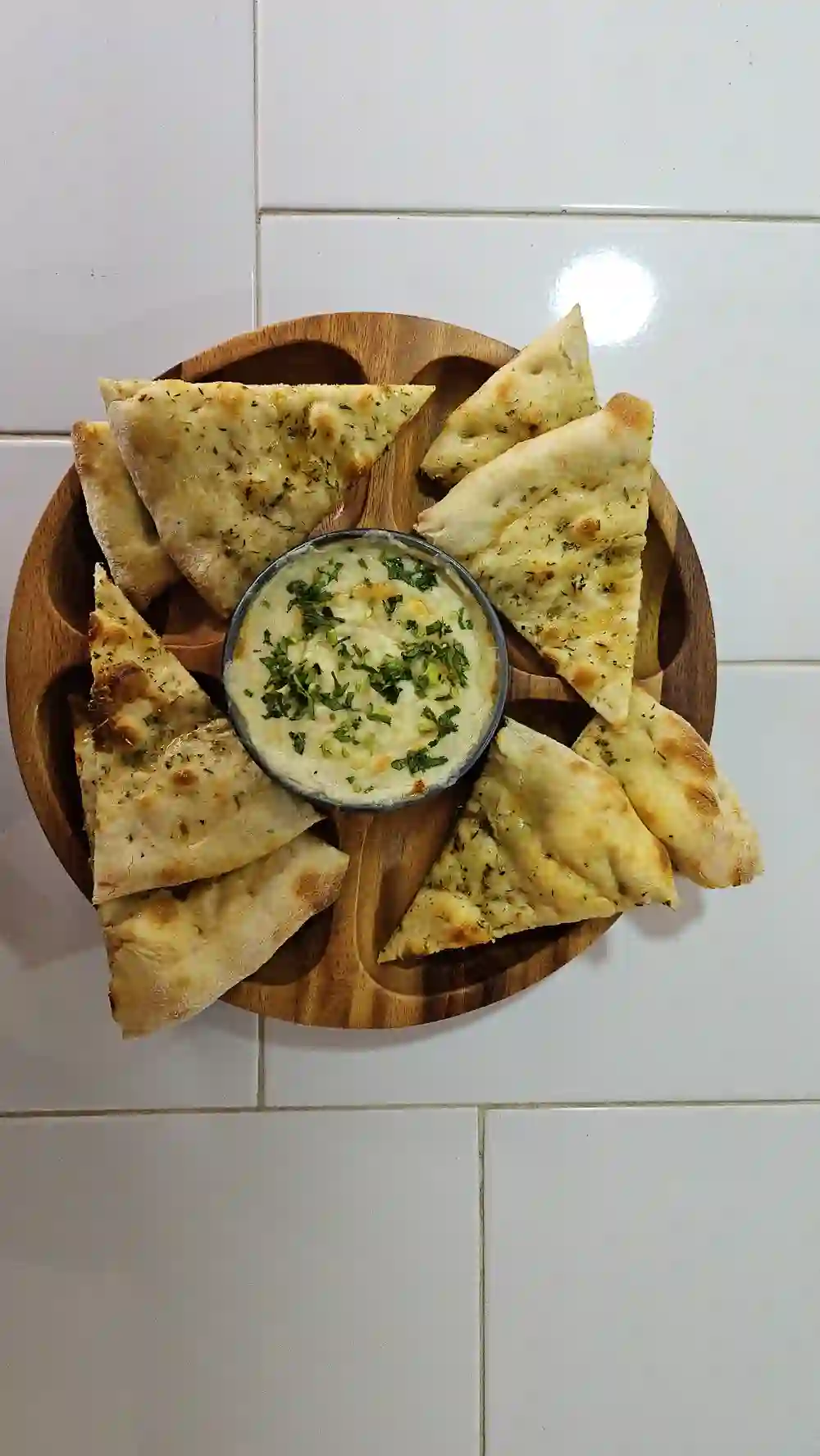 Pan de ajo en triángulos alrededor de un dip cremoso, sobre tabla de madera