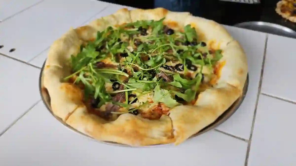 Pizza con arúgula y aceitunas negras, de orilla inflada, recién horneada